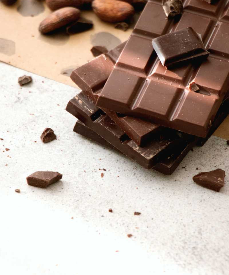 Chocolate blocks stacked haphazardly on top of each other with cacao beans scattered on top